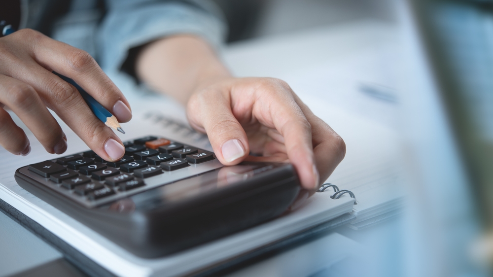 Close up woman hand using calculator to calculate home finance and writing note, accounting on table, budget management. Doing finance, budgeting and tax calculation, monthly expenses
